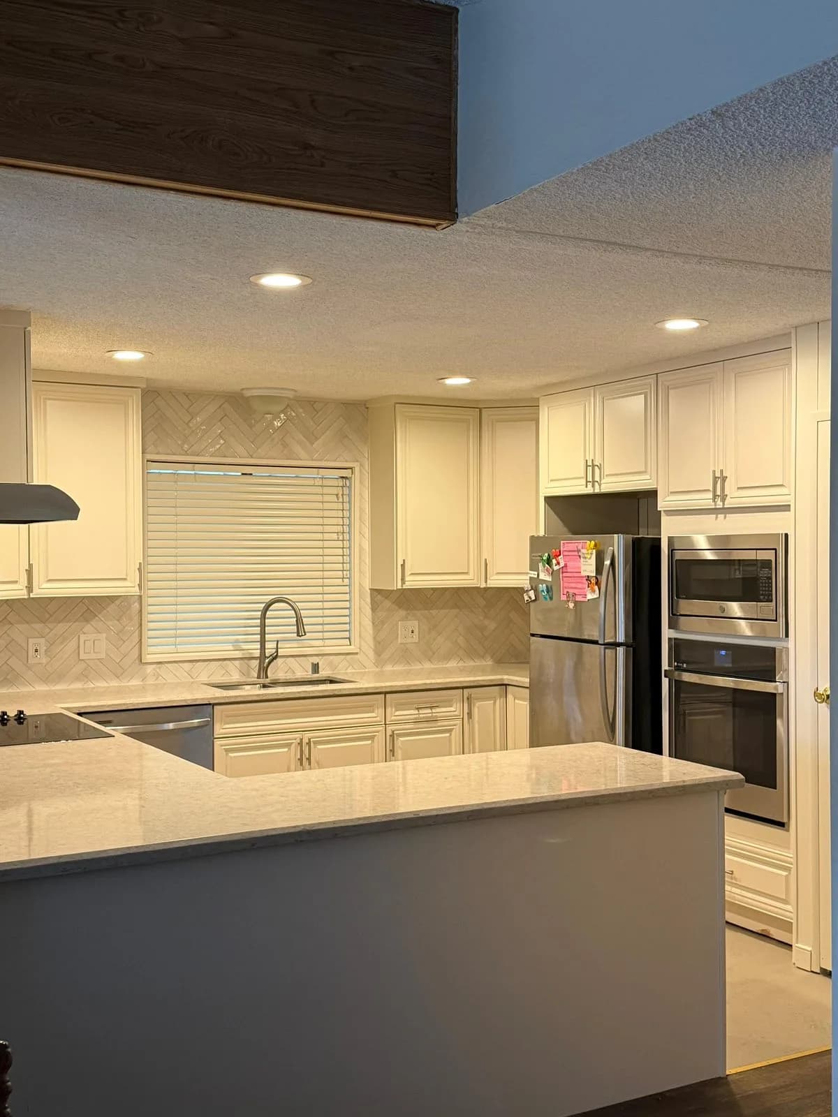 Remodeled white kitchen with herringbone tile backsplash, quartz peninsula, and built-in wall oven and microwave