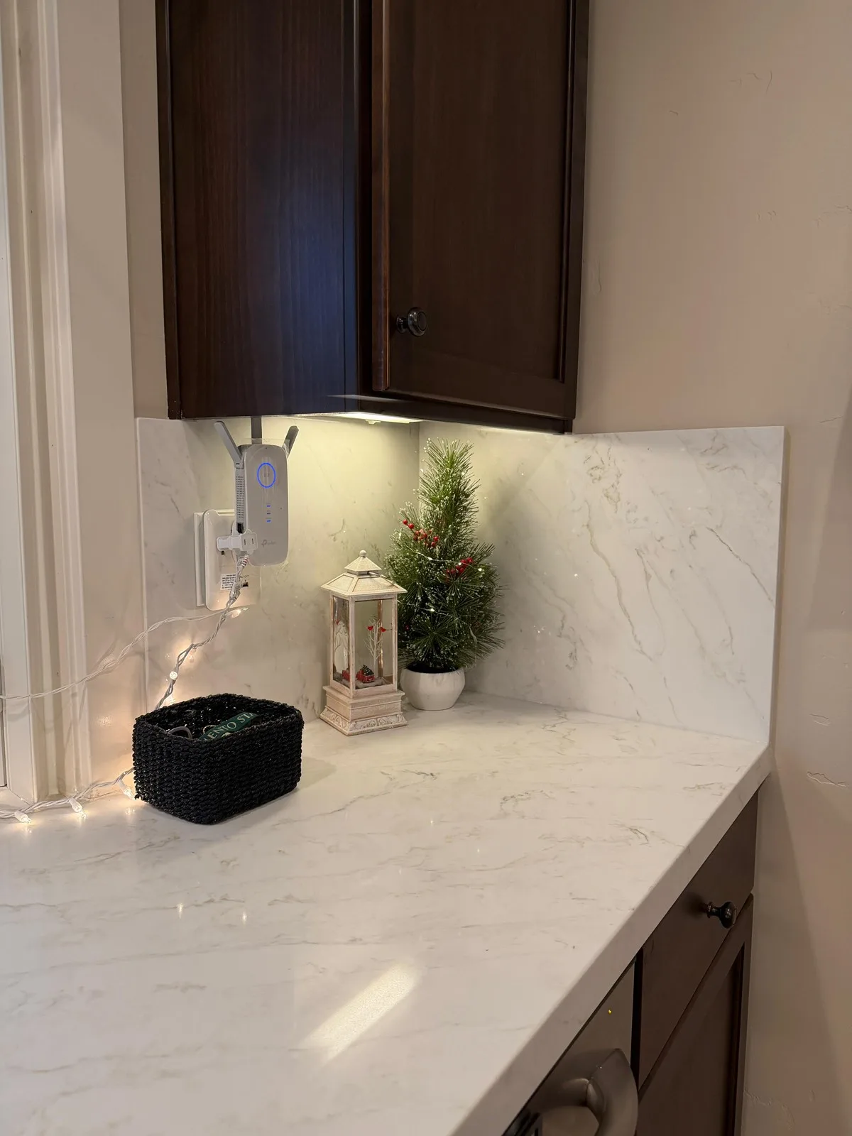 Under-cabinet lighting over marble-look quartz counters and backsplash in an espresso kitchen
