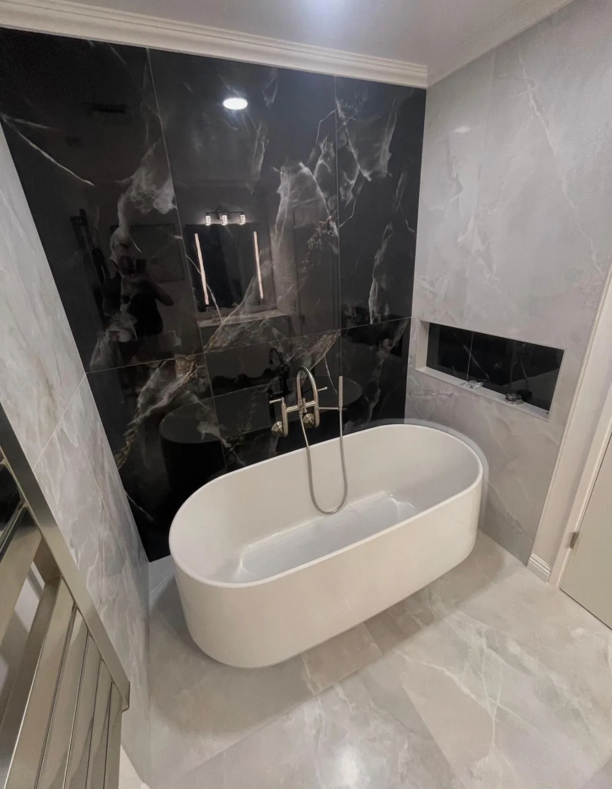 Freestanding oval tub with floor-mounted filler against a black marble-look accent wall