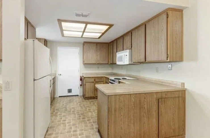Kitchen before remodel with honey oak cabinets, white appliances, and fluorescent box light