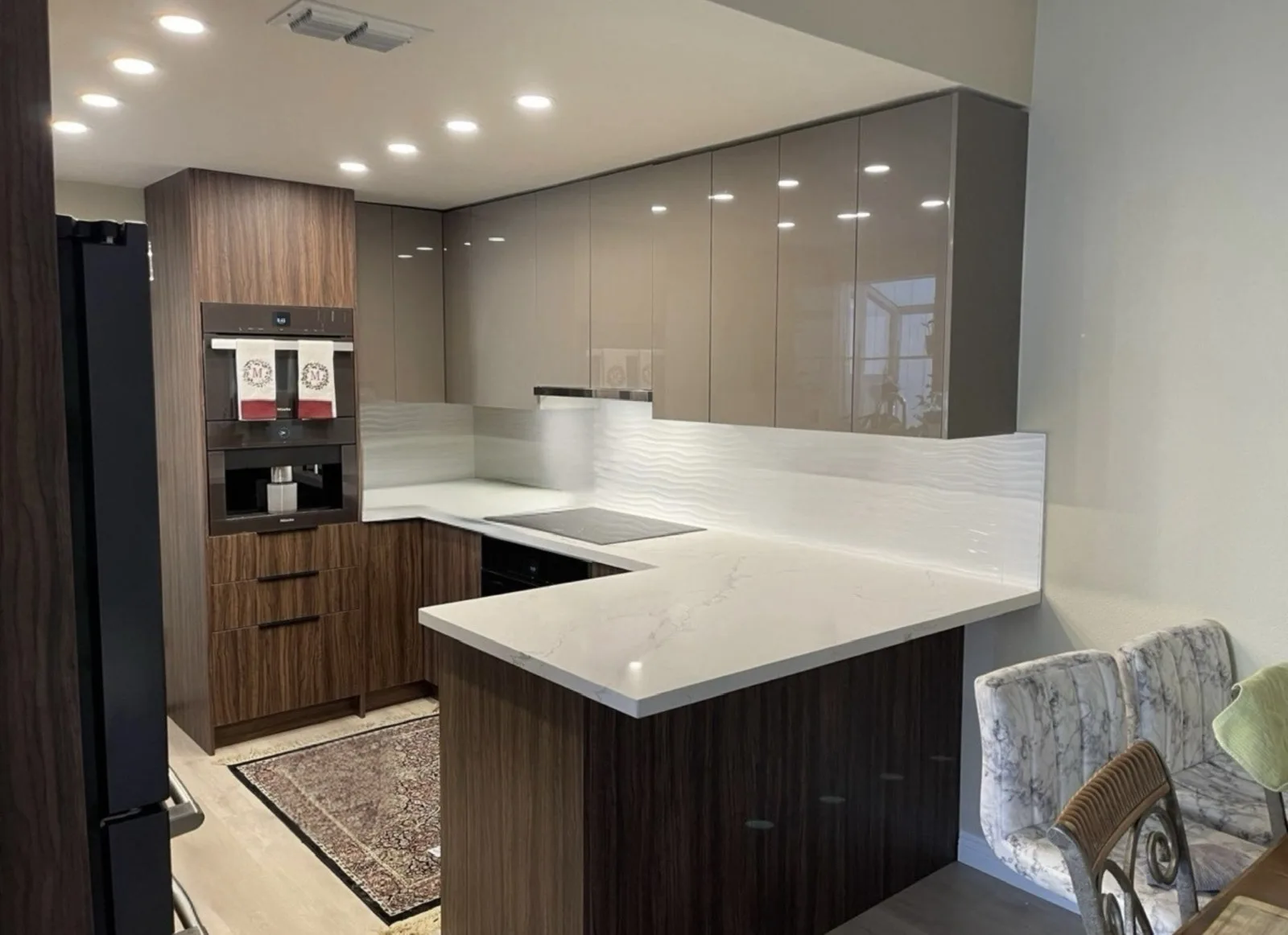 Remodeled U-shaped kitchen with veined quartz counters, black-glass cooktop, and built-in wall oven and coffee system